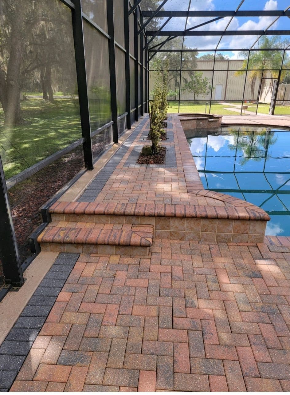 Clean paver patio beside a pool after pressure cleaning and sealing