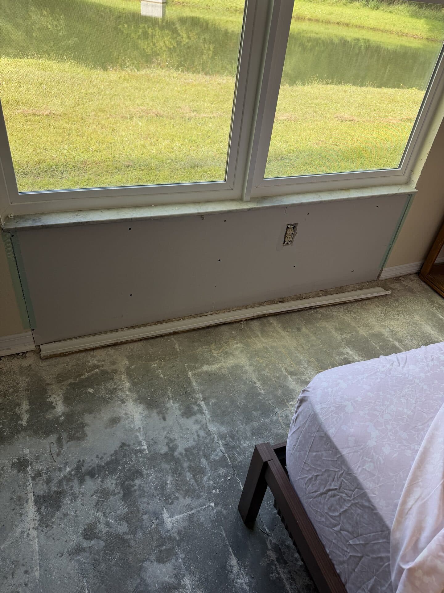 New drywall installed under a bedroom window with the floor taken down to the slab