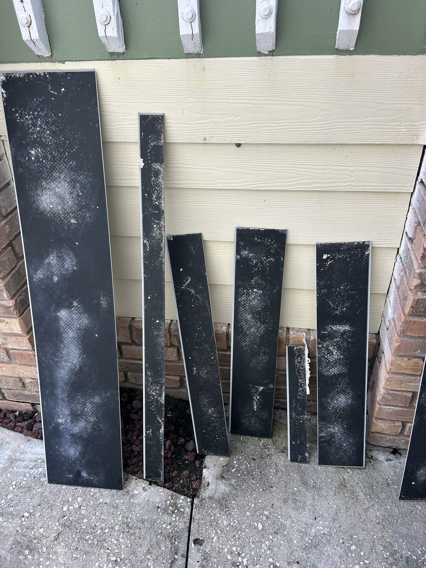 Removed vinyl planks leaned against the outside wall, mold growing across their backing