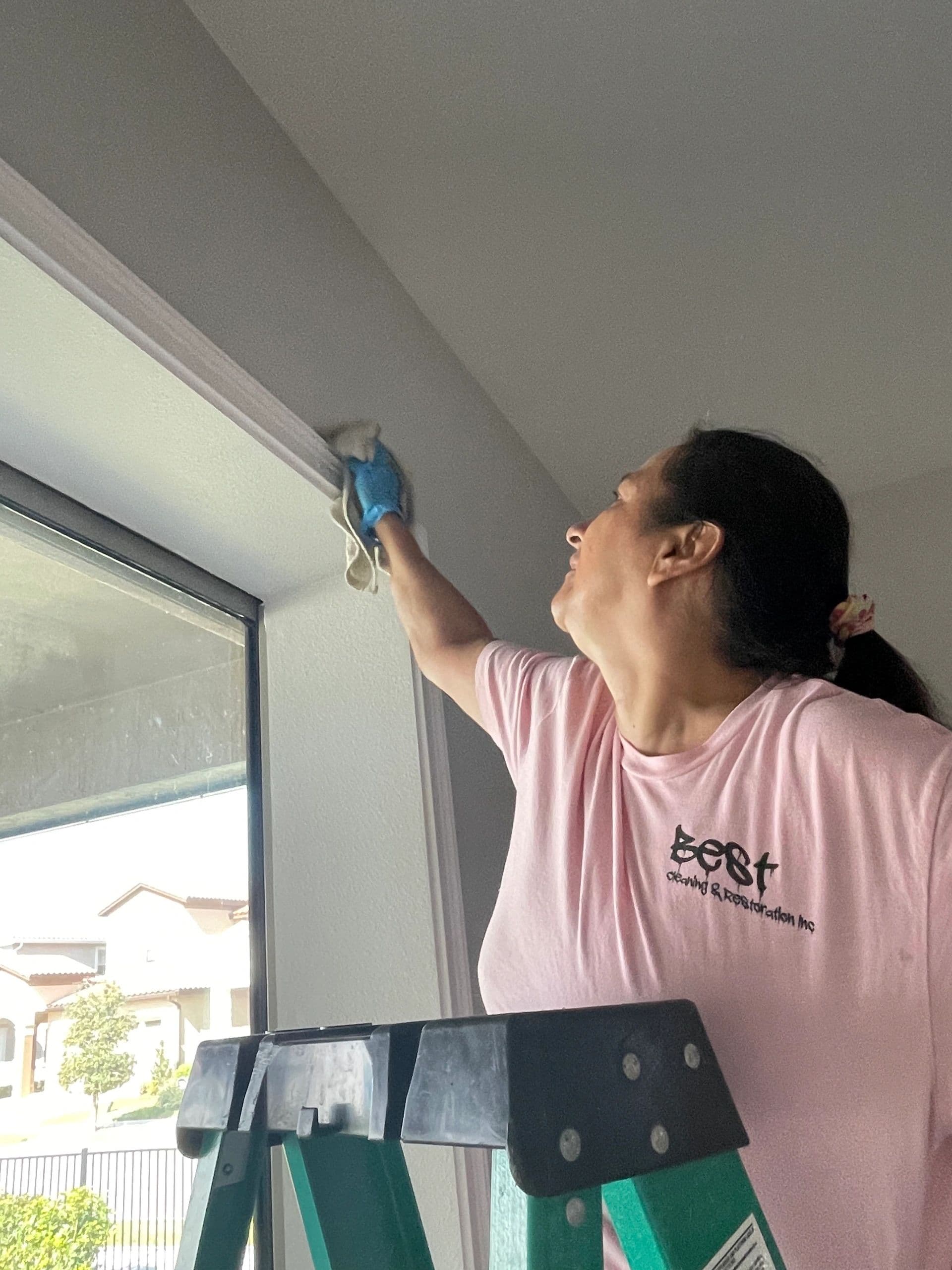 Best Cleaning & Restoration team member on a ladder detailing the top of a window frame during a post-construction cleanup